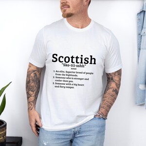 May include: White t-shirt with a black graphic design that defines the word "Scottish" as an elite, superior breed of people from the highlands, someone who is stronger and cooler than you, and someone with a big heart and fiery temper.