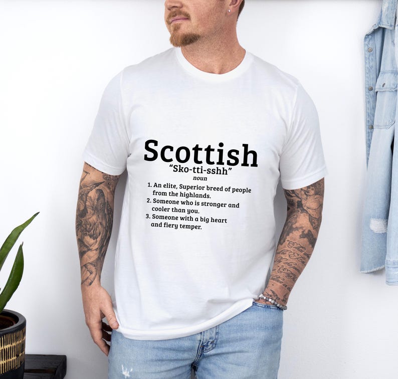 May include: White t-shirt with a black graphic design that defines the word "Scottish" as an elite, superior breed of people from the highlands, someone who is stronger and cooler than you, and someone with a big heart and fiery temper.