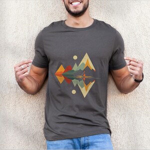 May include: A dark gray t-shirt with a geometric design of mountains and a lake reflecting the mountains. The design is in shades of orange, yellow, green, and blue.