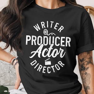 Può includere: T-shirt nero con testo bianco "Writer, Producer, Actor, Director". Il design include grafiche di bobina cinematografica e ciak. La maglietta è girocollo e a maniche corte.