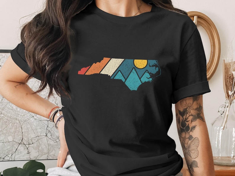 Black t-shirt with North Carolina outline featuring mountains and a sunset.