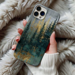 May include: A phone case featuring an abstract forest scene with green and gold trees against a gray background. The case has a matte finish and a camera cutout. The case is held in a person's hand.