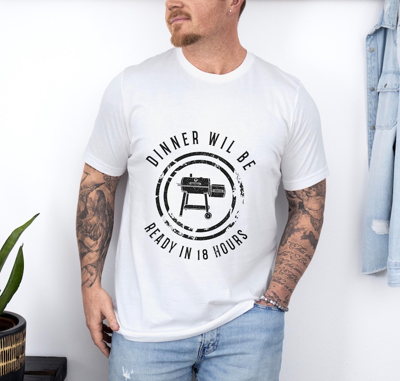 K&ouml;nnte beinhalten: Wei&szlig;es T-Shirt mit einer schwarzen Grafik eines Grills und dem Text "Dinner will be ready in 18 hours".