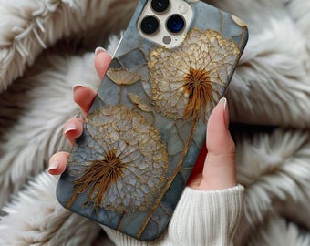 May include: A smartphone case with a floral design. The case features a detailed illustration of dandelions in shades of gold and white against a blue-grey background. The case has a glossy finish and a raised texture, adding depth to the design.