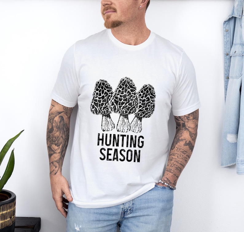 May include: White t-shirt with a black and white illustration of three morel mushrooms and the text "Hunting Season".