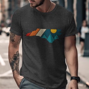 Dark t-shirt with North Carolina outline featuring mountain and sunset graphic.