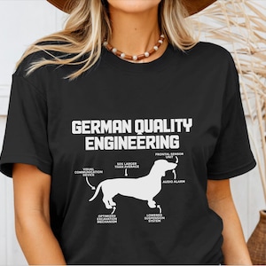 May include: Black t-shirt with a white dachshund silhouette and the text "German Quality Engineering". The dachshund is labeled with features like "Visual Communication Device", "50% Larger Than Average", "Frontal Sensor Unit", "Audio Alarm", "Optimized Excavation Mechanism", and "Lowered Suspension System".