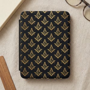 May include: Black and gold patterned tablet case featuring a repeating Masonic symbol design. The symbols include a compass, square, and the letter "G". The case is rectangular and appears to be made of a textured material.