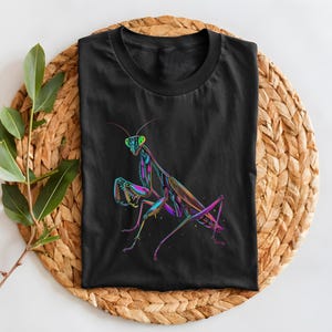 May include: Black t-shirt with a colorful graphic of a praying mantis. The mantis is outlined in black and filled with shades of pink, purple, green, and blue.
