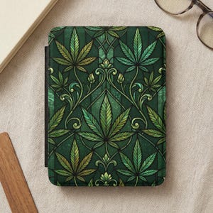 Op de afbeelding: Tablethoes met een groen en goud cannabisbladpatroon. Het ontwerp toont gedetailleerde bladeren en wervelende ranken tegen een donkergroene achtergrond. De hoes heeft een zwarte rug.