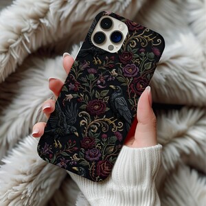 May include: A black smartphone case featuring a detailed pattern of dark purple roses, green foliage, and black ravens. The design includes intricate gold-colored swirling vines and stems set against a solid black background with a camera cutout.