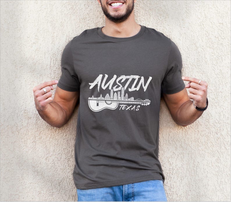 May include: A dark gray t-shirt with a white graphic design of the Austin, Texas skyline with a guitar. The text "Austin Texas" is printed below the skyline.