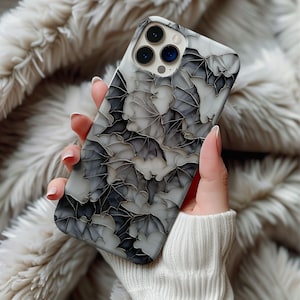 May include: A smartphone case featuring a repeating pattern of stylized bats in shades of gray and white. The case has a glossy finish and a raised design, with a camera cutout at the top. The overall theme is Halloween or gothic.