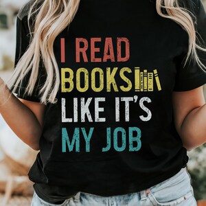 May include: Black t-shirt with a vintage-style graphic that reads "I read books like it's my job". The graphic features a stack of books in yellow and red.