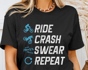 Peut inclure: T-shirt noir avec un motif blanc qui dit "Ride Crash Swear Repeat" avec une illustration de vélo bleu et un cercle bleu avec une flèche.