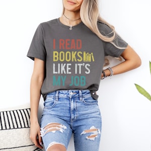 May include: A grey t-shirt with the text "I READ BOOKS LIKE IT'S MY JOB" in a vintage style font. The text is in red, yellow, and blue.