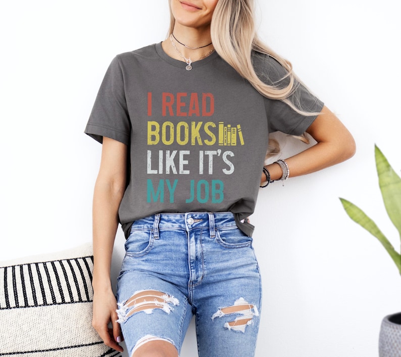 May include: A grey t-shirt with the text "I READ BOOKS LIKE IT'S MY JOB" in a vintage style font. The text is in red, yellow, and blue.