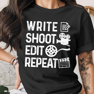 Könnte beinhalten: Schwarzes T-Shirt mit dem weißen Text "WRITE SHOOT EDIT REPEAT" und Symbolen für Notizblock, Filmkamera, Filmrolle und Klappe. Das Shirt hat einen Rundhalsausschnitt und kurze Ärmel.