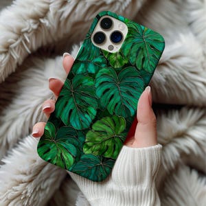 May include: A phone case featuring a vibrant green monstera leaf design with gold accents. The case has a glossy finish and a dark green background. The design is a repeating pattern of large tropical leaves, creating a lush, botanical aesthetic.