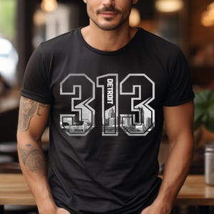 May include: Black t-shirt with a white graphic of the numbers 313 with the word "DETROIT" inside the 1. The graphic is a cityscape.