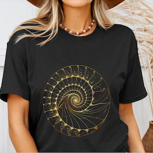 May include: Black t-shirt featuring a golden spiral design. The intricate artwork is centered on the shirt and appears to be a detailed illustration of a nautilus shell or a similar geometric pattern. The design is rendered in shades of gold.
