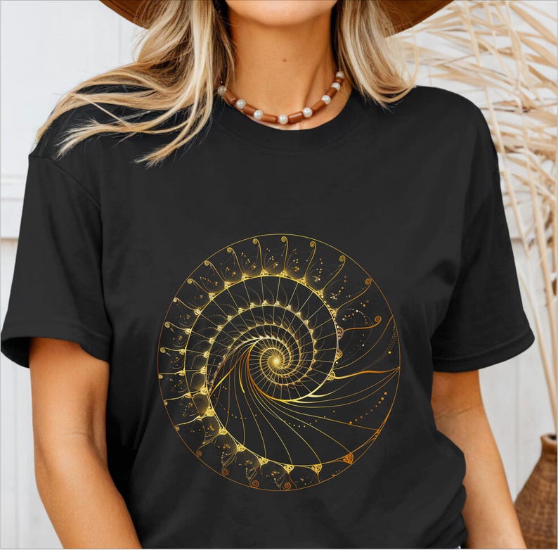 May include: Black t-shirt featuring a golden spiral design. The intricate artwork is centered on the shirt and appears to be a detailed illustration of a nautilus shell or a similar geometric pattern. The design is rendered in shades of gold.