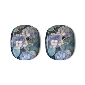 May include: Two oval decorative items with a floral design. They display blue and white hydrangeas with green leaves and gold accents on a dark blue backdrop. The objects are set against a white background.