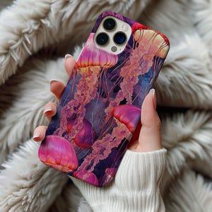 Puede incluir: Una funda para teléfono con un fondo morado oscuro y un diseño de medusas rosas y moradas. La lente de la cámara es visible en la parte posterior de la funda.