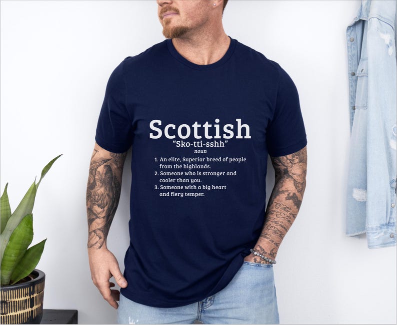 May include: A navy blue t-shirt with white text that reads "Scottish "Sko-tti-sshh" noun 1. An elite, Superior breed of people from the highlands. 2. Someone who is stronger and cooler than you. 3. Someone with a big heart and fiery temper."