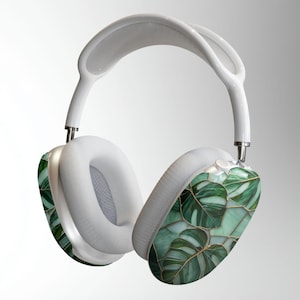 Könnte beinhalten: Weiße Over-Ear-Kopfhörer mit einem grünen und goldenen Blättermuster auf den Ohrmuscheln. Das Kopfband und die Ohrpolster sind weiß. Das Design zeigt ein botanisches Thema mit einer modernen Ästhetik.