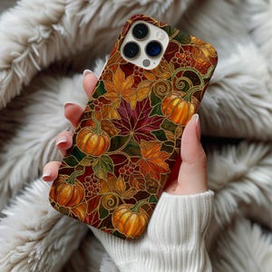May include: A smartphone case featuring a stained glass style pattern of orange pumpkins, red and yellow maple leaves, and small red berries. The design uses dark outlines to separate the colorful autumn elements across the entire back surface.