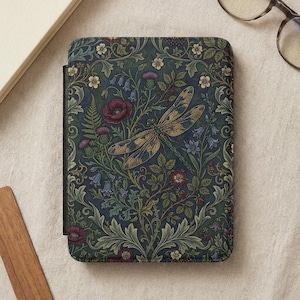 Puede incluir: Una funda decorativa con un diseño floral y de libélula. La funda tiene un fondo azul oscuro con un patrón de flores, hojas y una libélula en tonos dorados, verdes y burdeos. La funda es rectangular y parece ser para un lector electrónico.