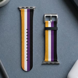 May include: A watch band featuring a vertical striped pattern in yellow, white, purple, and black. The band includes a silver-toned metal buckle and attachment hardware, with a series of adjustment holes running down the center of the longer strap.