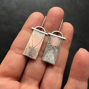 May include: A pair of silver earrings with a detailed design of a centipede. One earring is copper and the other is silver.