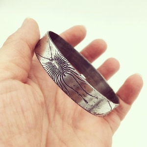 Pode incluir: Um bracelete de prata com uma superfície texturizada e um design detalhado de uma centopeia.