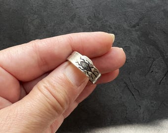 May include: A silver ring with a detailed design of a beetle on the band.