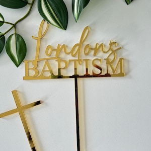 May include: Gold acrylic cake topper with the text "Londons Baptism" and a gold cross.