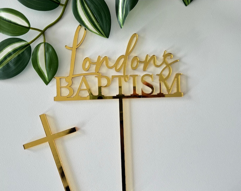 May include: Gold acrylic cake topper with the text "Londons Baptism" and a gold cross.