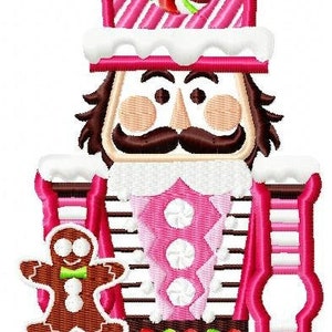 May include: A pink and white embroidered nutcracker with a gingerbread man. The nutcracker has a hat with a candy swirl, a white face, and a brown mustache. The gingerbread man is holding a tray.