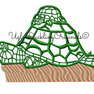 May include: Green embroidered design of two stacked turtles on a brown wooden surface. The design is outlined in black and has a detailed shell pattern.