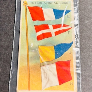 以下が含まれることがあります： 上部に「INTERNATIONAL CODE」というテキストが書かれたビンテージカード。4つの旗がポールに掲げられており、その横にE、F、G、Hの文字が書かれている。