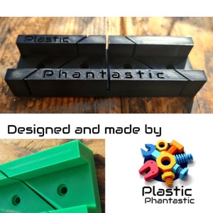 Könnte beinhalten: Zwei schwarze Kunststoff-Gehrungsklemmen mit dem Aufdruck "Plastic Phantastic". Die Klemmen sind so konzipiert, dass sie Holz in einem 90-Grad-Winkel halten.