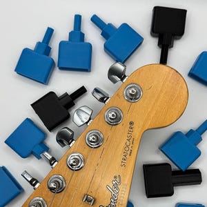 May include: A Fender Stratocaster guitar headstock with tuning pegs, surrounded by blue and black guitar string winders. The guitar headstock is made in Japan. The string winders are designed for quick string changes.
