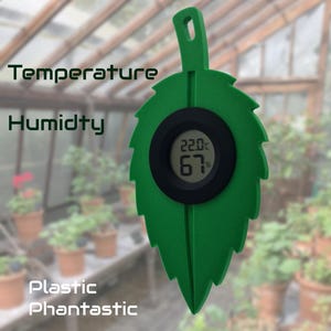 Puede incluir: Un sensor de temperatura y humedad en forma de hoja verde, que muestra 22,0°C y 67%. El sensor tiene las palabras "Temperature", "Humidity", "Plastic" y "Phantastic" impresas.