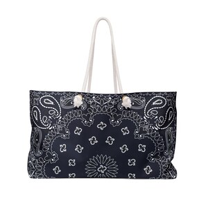 May include: A large tote bag with a navy blue paisley pattern and white accents. The bag has white rope handles and is designed for carrying items. The bag's design is reminiscent of a bandana.