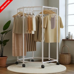 May include: A white rolling clothing rack with various garments hanging on wooden hangers. The clothes include skirts, tops, and sweaters in neutral colors. The rack is on a round, cream-colored rug.