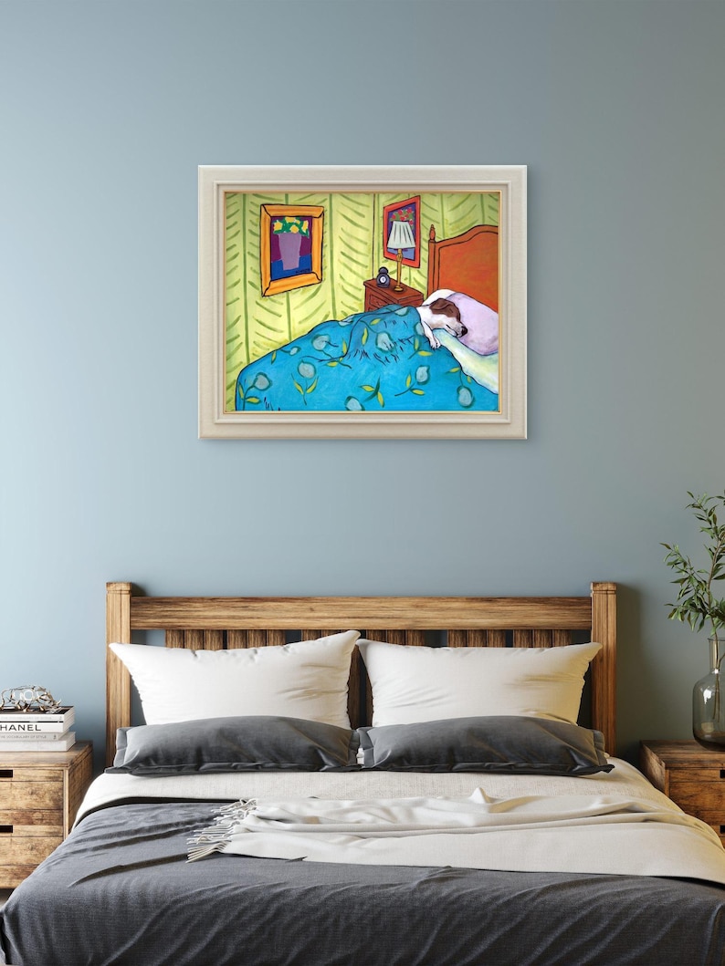 May include: A framed art print depicting a bedroom scene with a dog sleeping under a blue patterned blanket. The room features yellow walls with a green chevron pattern, a wooden headboard, a bedside table with a lamp, and two framed pictures.