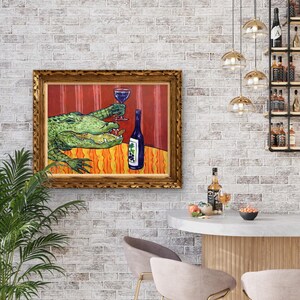 May include: A framed painting featuring a green alligator holding a wine glass filled with red liquid, positioned next to a blue wine bottle with a grape label. The scene is set against a red striped background and an orange patterned tablecloth.