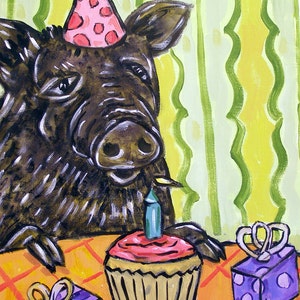 May include: A black and brown wild boar wearing a pink and white polka dot party hat sits at a table with a cupcake and two purple wrapped gifts. The cupcake has a single blue candle and pink frosting.