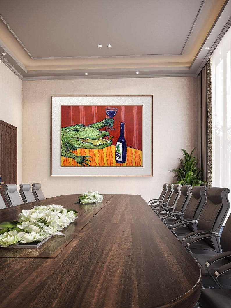 May include: A framed wall art print featuring a green alligator sitting at a table with an orange patterned tablecloth. The alligator holds a glass of red wine, and a blue wine bottle with a grape label sits on the table against a red striped background.